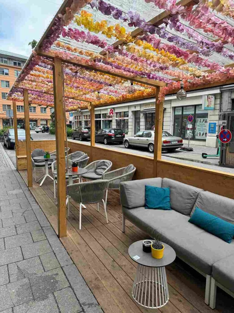 Blick auf die Terrasse des Cafe Nil München: Sofas und und Stühle am Rande der Straße