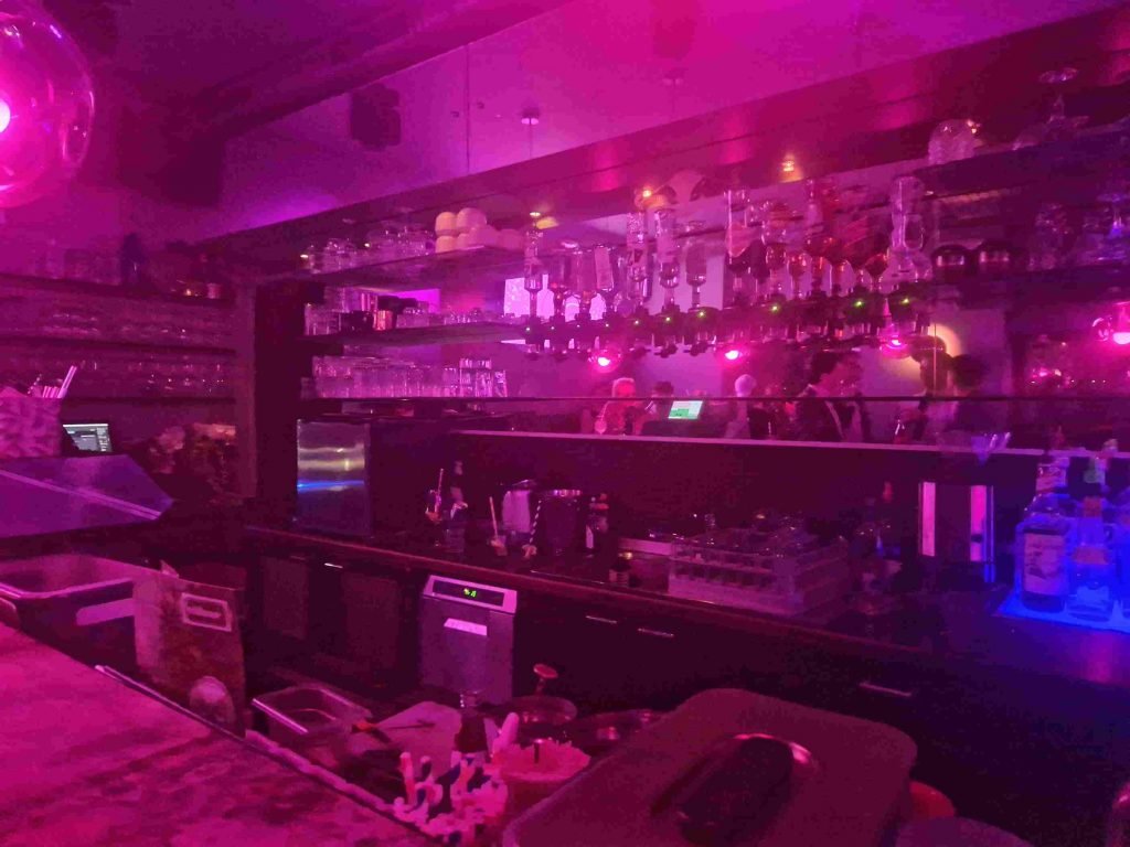 Blick auf die in lilanem Licht getauchte Theke der Village Bar Wien