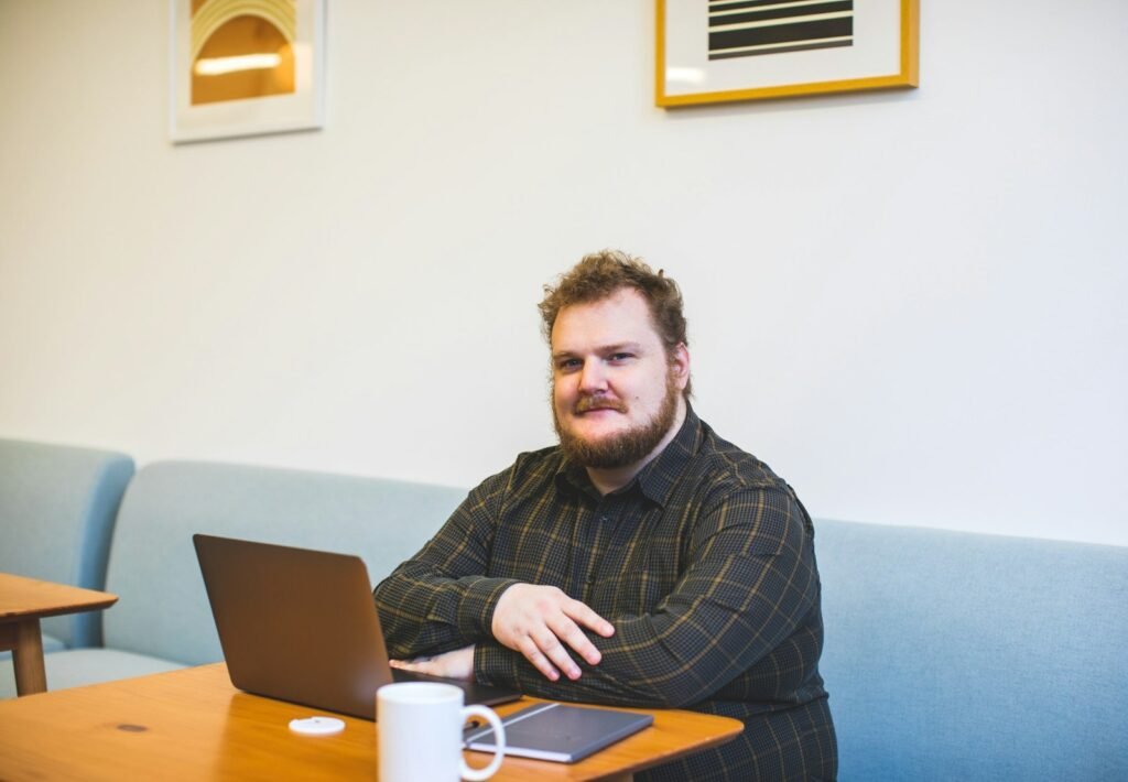 Mann mit Bart sitzt mit Laptop an einem Tisch