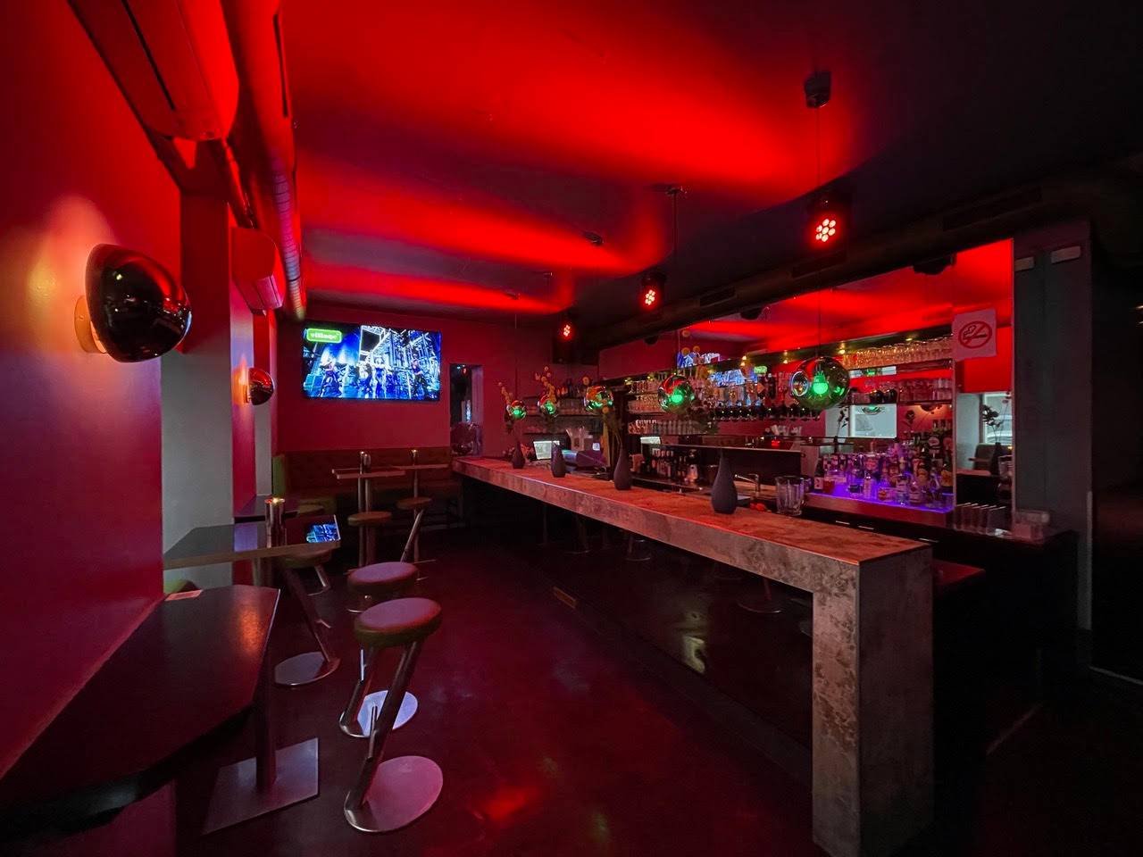 Bar der Village Bar in Wien in rotem Licht mit Theke und Barhockern